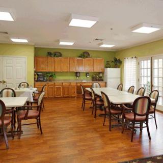 A dining area with multiple tables and chairs, featuring a kitchen at the back.