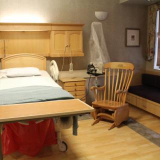 A cozy hospital room with a patient bed, rocking chair, and wooden furnishings.