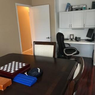 A home office setup featuring a desk with a computer and a table with a chessboard.