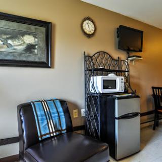 A cozy hotel room corner featuring a comfortable chair, a mini refrigerator, microwave, and a television.