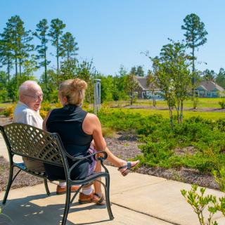 A couple sits on a bench enjoying the sunny view in a park.