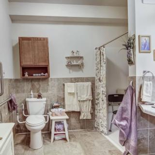 A neatly arranged bathroom featuring a toilet, shower with curtain, and various towels and decor.