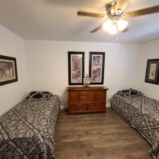 A bedroom with two single beds, a ceiling fan, wooden dresser, and framed artwork on the walls.