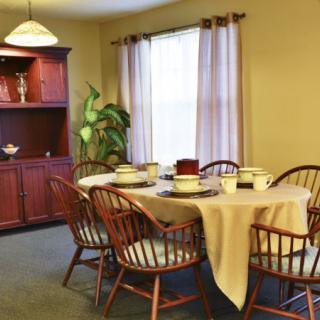 A cozy dining room with a set table and wooden chairs, featuring a cabinet and curtains.