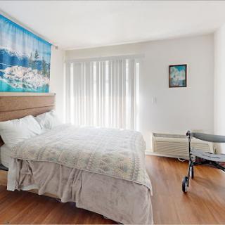 A bright and inviting bedroom featuring a cozy bed, window blinds, and wall art.