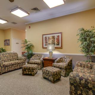 A cozy waiting room with patterned sofas, chairs, and decorative plants.