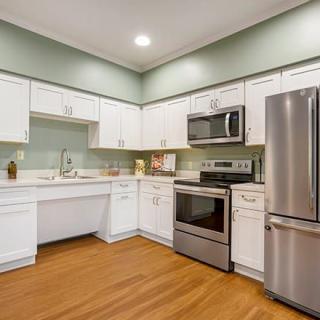 A modern kitchen with white cabinets, stainless steel appliances, and wood flooring.