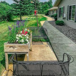 A peaceful patio area with a flower planter, bench seating, and a pathway alongside a building.