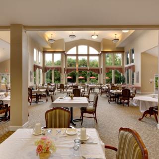 A spacious and elegant dining room with large windows, featuring neatly arranged tables and chairs.
