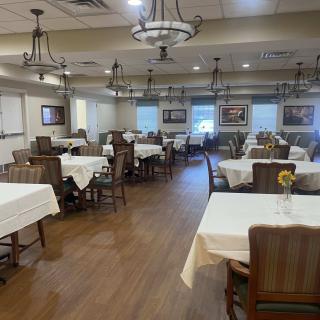An empty dining room with set tables and wooden chairs, decorated with chandeliers.
