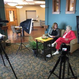 A cozy indoor setting for an interview featuring two women seated on a sofa, with filming equipment set up.