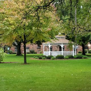A serene park featuring a white gazebo surrounded by lush greenery and trees in autumn.