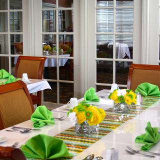 A beautifully set dining table with green napkins and yellow floral centerpieces.