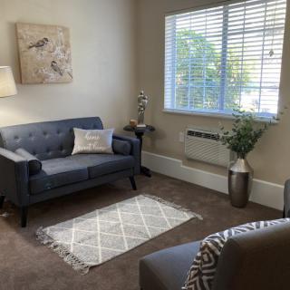 A cozy living room with modern decor, featuring a couch, armchair, and window letting in natural light.