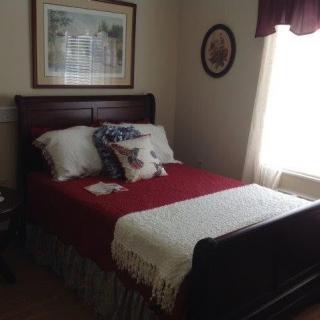 A cozy bedroom with a neatly made bed, decorated with pillows and a throw blanket, illuminated by natural light from a window.