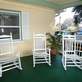 A cozy porch with three white rocking chairs and a potted plant.