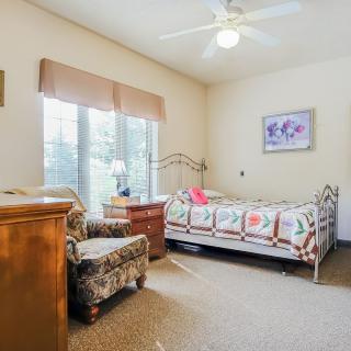 A cozy bedroom with a daybed, armchair, and large windows letting in natural light.