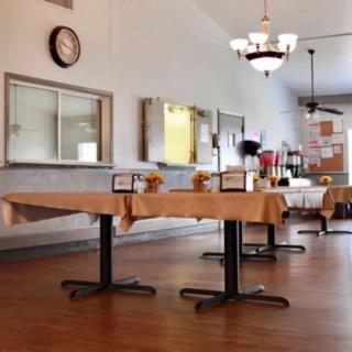 A spacious dining area with neatly arranged tables and chairs, featuring a chandelier and a wall clock.