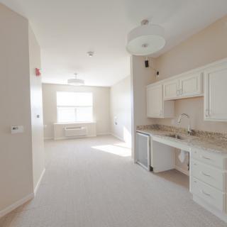 A bright and empty apartment interior featuring a small kitchen area with white cabinets.
