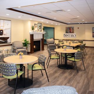 A modern dining area with round tables and cushioned chairs, featuring a fireplace and decorative elements.