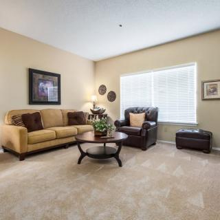 A cozy living room with a yellow sofa, brown armchair, and a central coffee table on a carpeted floor.