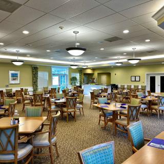 An empty dining room with neatly arranged tables and chairs, featuring soft lighting and large windows.