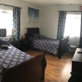 A cozy bedroom with twin beds, patterned bedding, and natural light filtering through the windows.