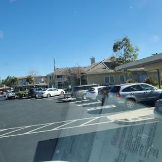 A view of a busy parking lot with various cars parked outside a building under a clear blue sky.
