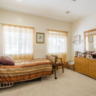 A cozy bedroom with a single bed, dresser, and soft lighting from the windows.