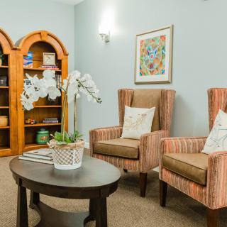 A cozy living room with two striped armchairs, a wooden bookshelf, and a round table decorated with flowers.