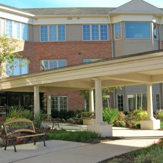 A sunny view of a residential building with landscaped greenery and an entrance canopy.