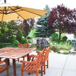 A serene outdoor patio area complete with wooden furniture, a sun umbrella, and a lush garden.