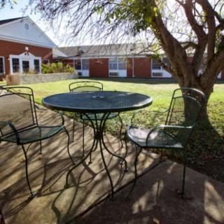 A sunlit patio area with a metal table and chairs surrounded by a garden.