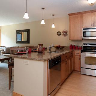 A modern kitchen interior featuring wood cabinets, stainless steel appliances, and an adjacent dining area.