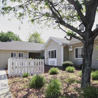 A well-maintained single-story house with a fenced front yard, surrounded by trees and landscaped garden.
