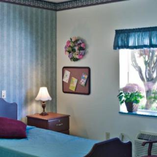 A cozy bedroom with a bed, side table with a lamp, and a window featuring floral decor.