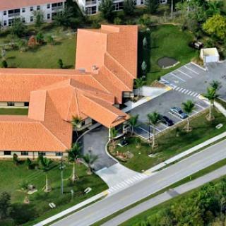 An aerial view of a residential building with an orange roof, surrounded by landscaped areas and palm trees.