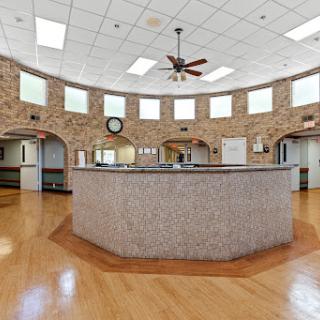 A spacious and well-lit reception area featuring a rounded front desk and elegant wooden flooring.