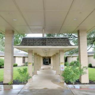 A covered entrance with columns leading to a building surrounded by greenery.