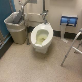 A bathroom with a toilet, trash can, walker, and toilet paper holder.