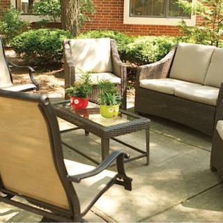 A cozy outdoor patio setup with cushioned chairs and a central table, surrounded by greenery.