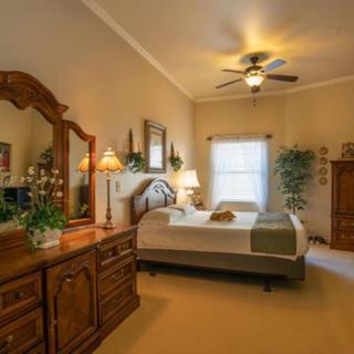A cozy bedroom with classic wooden furniture, including a bed, dresser, and nightstands, complemented by a ceiling fan and decorative plants.