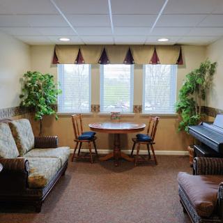 A cozy living room setup featuring a sofa, a small dining table with chairs, and a piano, complemented by some indoor plants.