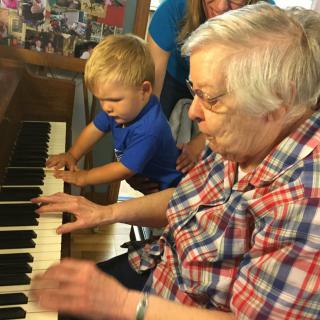 An elderly person and a child playing the piano together, sharing a musical moment.