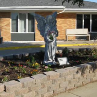 An angel statue stands in a garden outside a brick building.