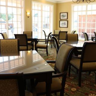A sunlit dining room with tables and chairs arranged neatly by the windows.