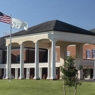 A building with large columns and flags in front, surrounded by a well-maintained lawn.