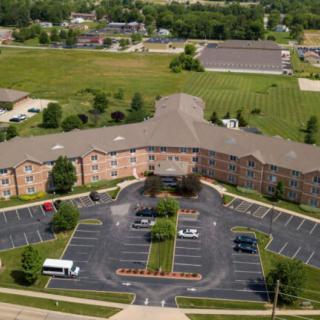 Aerial view of a large building with a parking lot and surrounding greenery.