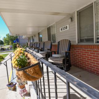 A row of rocking chairs on a porch with hanging flower baskets.