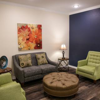 A modern living room featuring a gray sofa, green armchairs, and colorful artwork on the wall.